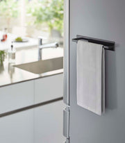 Yamazaki Home Magnetic Kitchen Towel Hanger on a stainless-steel fridge with a white towel draped over it in a modern kitchen setting.
