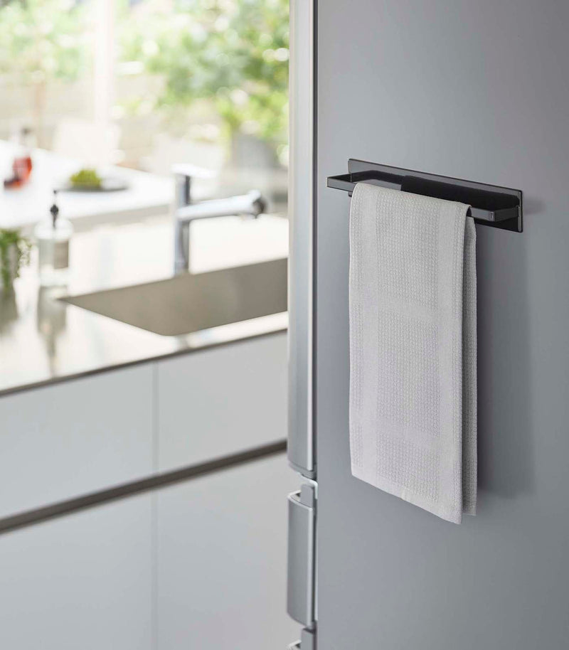 Yamazaki Home Magnetic Kitchen Towel Hanger on a stainless-steel fridge with a white towel draped over it in a modern kitchen setting.