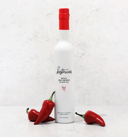 Kosterina - Spicy Red Pepper Olive Oil (375ml) bottle beside fresh red peppers, ideal for adding subtle spice to dishes.