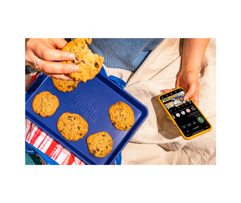 Hand holding Great Jones | Little Sheet - Pepper with a freshly baked cookie, showcasing its nonstick surface, ideal for small batch baking.