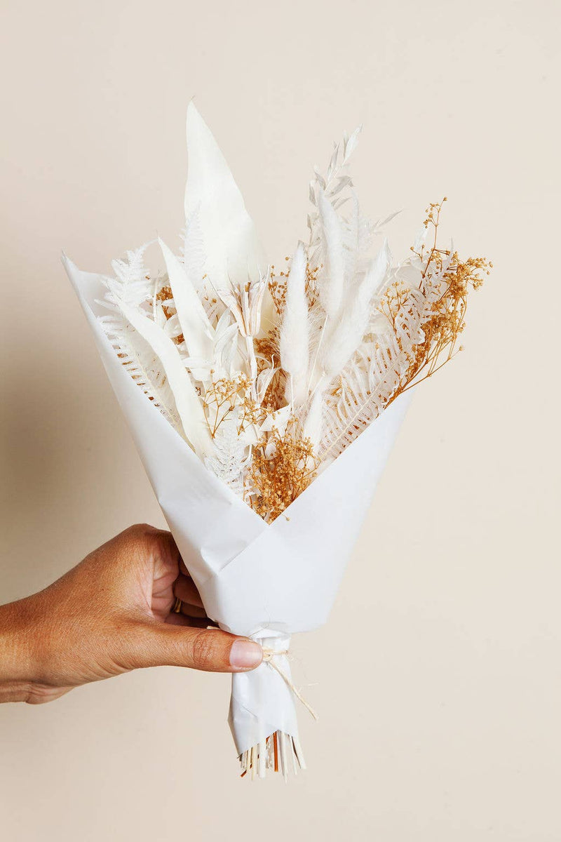 Idlewild Floral Co. - Snow Dried Flower Bouquet held in hand, featuring white-bleached ferns, plume grasses, and seed heads, wrapped in white paper and twine.