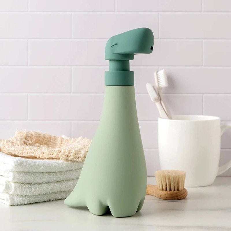 OTOTO - Soapasaurus soap dispenser alongside white towels and a mug with a brush, offering a whimsical touch for your bathroom essentials.