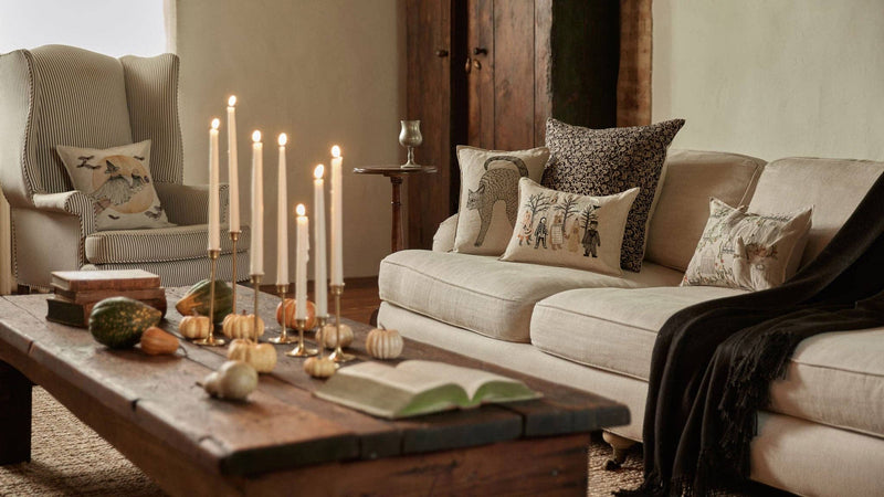 Coral & Tusk - Scaredy Black Cat Pillow on a cozy autumn-themed sofa, surrounded by seasonal decor and brass candlesticks on a rustic coffee table.