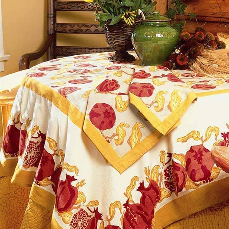 Couleur Nature - Pomegranate Yellow & Red tablecloth with stylized pomegranates, accented by a wicker basket of flowers, enhancing dining spaces with French-inspired charm.