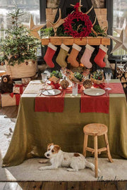 MagicLinen - Embroidered Christmas Stockings hang on a stone fireplace, enhancing a cozy dining nook with festive decor and a lounging terrier.