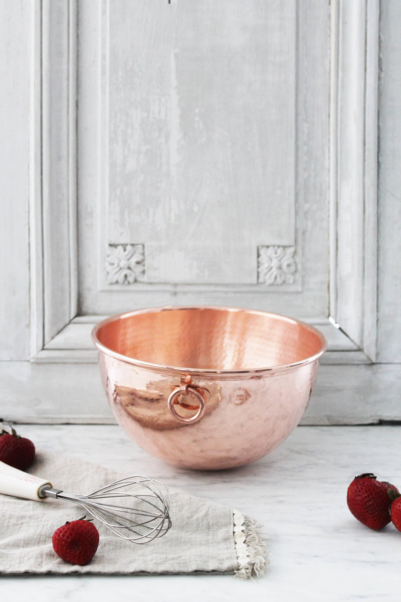 Coppermill Kitchen LLC - Coppermill Vintage Inspired Mixing Bowl with handle, set on marble, accompanied by a whisk and strawberries, embodying elegance and warmth in cooking.