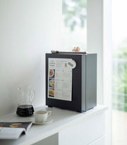 Yamazaki Home | Bread Box in matte-black on a white sideboard, featuring a handle and hinged side. Holds a recipe magnet, with snacks and coffee nearby.