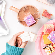 Cozy hot-cocoa scene featuring Malvi Mallow Cotton Candy 4-Pack Marshmallows, artistically sprinkled and skewered, surrounded by a delightful marshmallow variety on a pink plate.