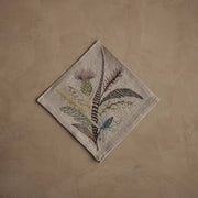 Coral & Tusk - Thistle Dinner Napkin featuring embroidered thistle, greenery, and feathers in muted tones on natural linen, perfect for seasonal table decor. Measures 20 × 20.