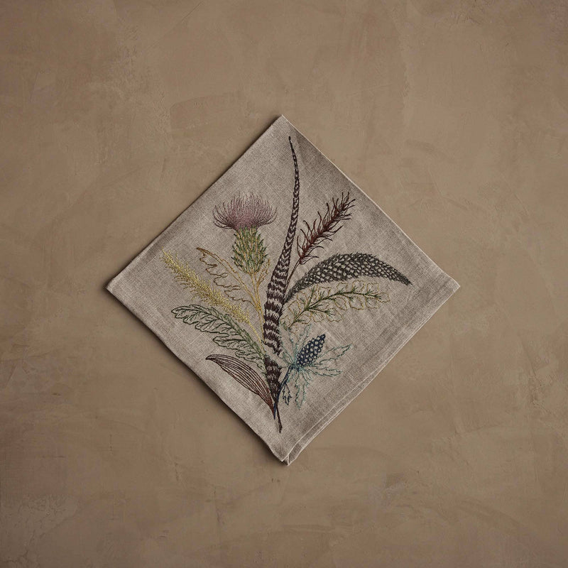 Coral & Tusk - Thistle Dinner Napkin featuring embroidered thistle, greenery, and feathers in muted tones on natural linen, perfect for seasonal table decor. Measures 20 × 20.