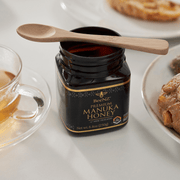 BeeNZ Premium Manuka Honey with a bambu® Bamboo Tea Spoon atop, flanked by tea and pastries, ideal for eco-friendly kitchen and gift setups.