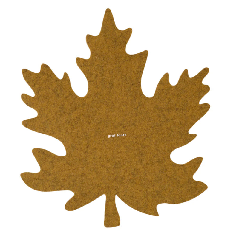 Graf Lantz Merino Wool Autumn Leaf Trivet - Ochre, a brown felt trivet shaped like a leaf, designed to protect surfaces while showcasing dishes.