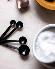 Farmhouse Pottery - Stowe Measuring Spoons in brushed gold on a countertop, with a bowl of coarse salt and garlic nearby, showcasing elegant kitchen essentials.