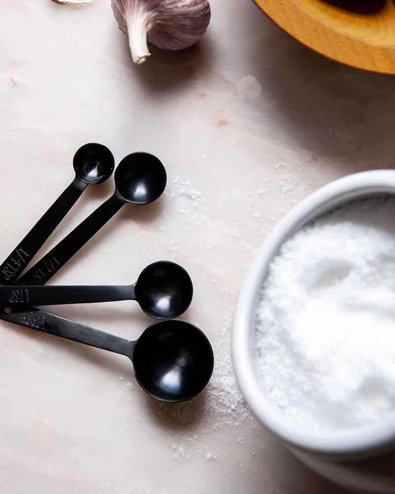Farmhouse Pottery - Stowe Measuring Spoons in brushed gold on a countertop, with a bowl of coarse salt and garlic nearby, showcasing elegant kitchen essentials.