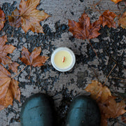 Among the Flowers - Essential oil candle | HOLIDAY: Hearth, unlit, on damp pavement with scattered maple leaves, next to dark green rubber boots.
