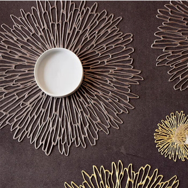 Chilewich | Bloom Placemat in Gunmetal, featuring a chrysanthemum-inspired openwork design, displayed on a brown surface, suitable as a decorative base or charger.