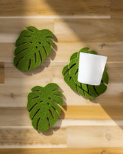 Graf Lantz Merino Wool Monstera Coaster Set displayed on a wooden surface, featuring green leaves for an organic touch to elegant dining settings.