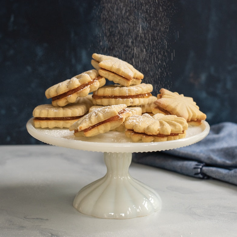 Nordic Ware | Pretty Pleated Cookie Stamps displayed with cookies on a white plate, showcasing intricate star, diamond, and floral imprints.