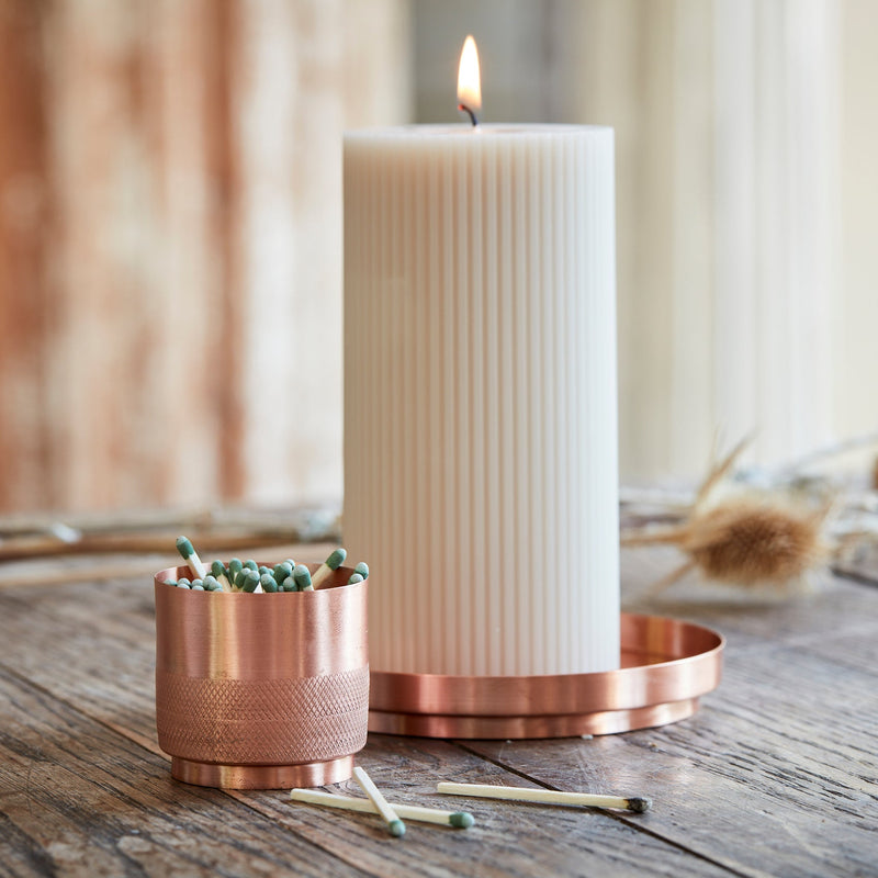 The Floral Society | Match Strike and Holder, a handmade copper vessel with textured surface, sits on a rustic table alongside a lit candle and spent matches.
