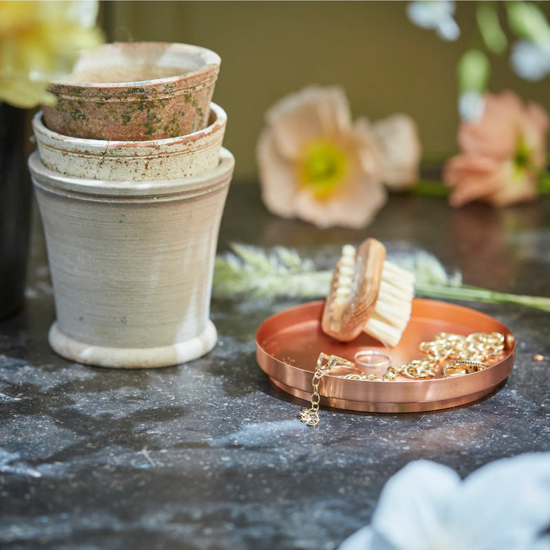 The Floral Society Aura Plate, a copper-plated tray, elegantly holds a scrub brush and gold jewelry, showcasing its versatile, handcrafted design.