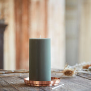 The Floral Society | Aura Plate: A copper-toned tray holds a tall, ribbed green pillar candle, ideal for safe burning or as a decorative accent on any tabletop.
