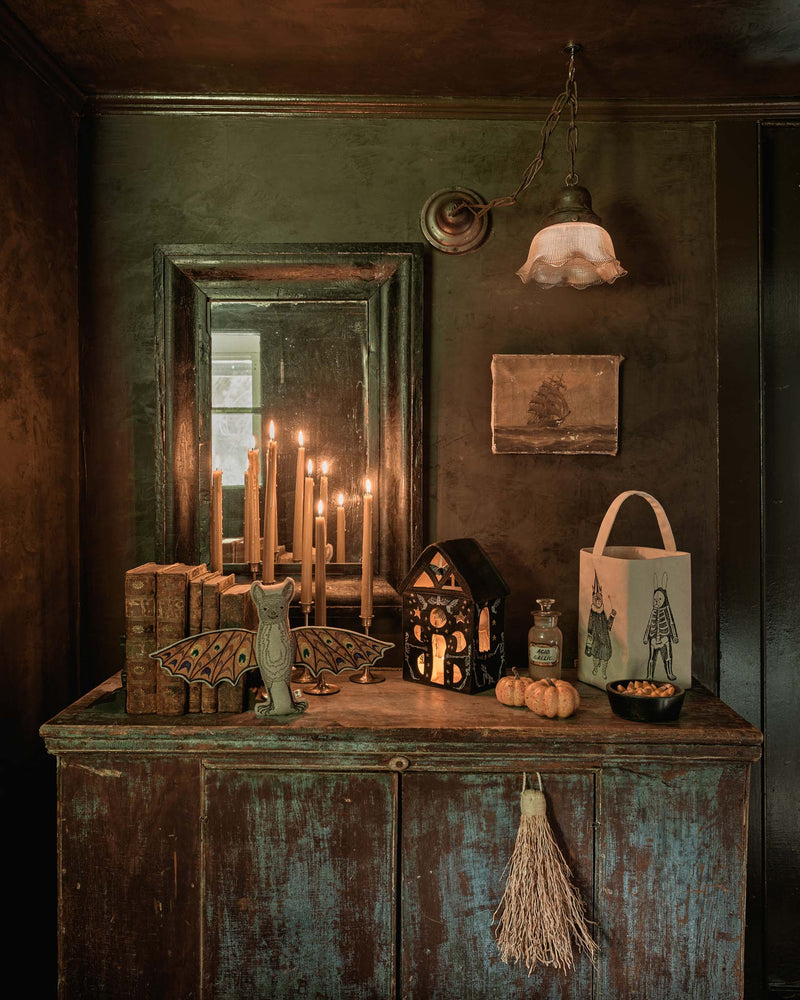 Coral & Tusk | Bat Surprise Doll with butterfly wings open, displayed on a moody Halloween-style sideboard with candles, lantern, and decorative items.