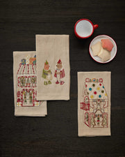 Coral & Tusk | Toy Workshop Tea Towel featuring festive gingerbread-house designs and caroling bears, styled with a red-rimmed mug and plate of sugar-coated cookies.