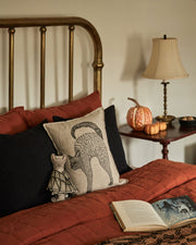 Coral & Tusk | Bat Surprise Doll nestled on a rust-orange quilted bed, with wings closed, amidst autumn-themed décor including pillows, a lamp, and decorative pumpkins.
