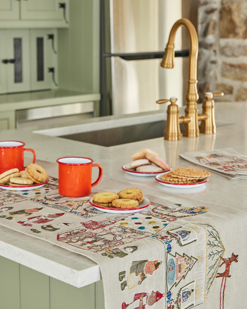 Coral & Tusk | Toy Workshop Tea Towel adorning a festive kitchen island with red-rimmed mugs, cookies, and pale green cabinetry in a cozy Athens Cooks setting.