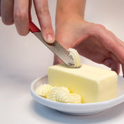 Microplane Butter Blade effortlessly curls butter with its unique blade, shown here creating decorative curls on a butter stick, ideal for spreading on baked goods.
