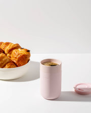 W&P - Ceramic Reusable Coffee Mug 16oz: Charcoal next to a bowl of croissants, showcasing its stylish, eco-friendly design with a silicone sleeve.