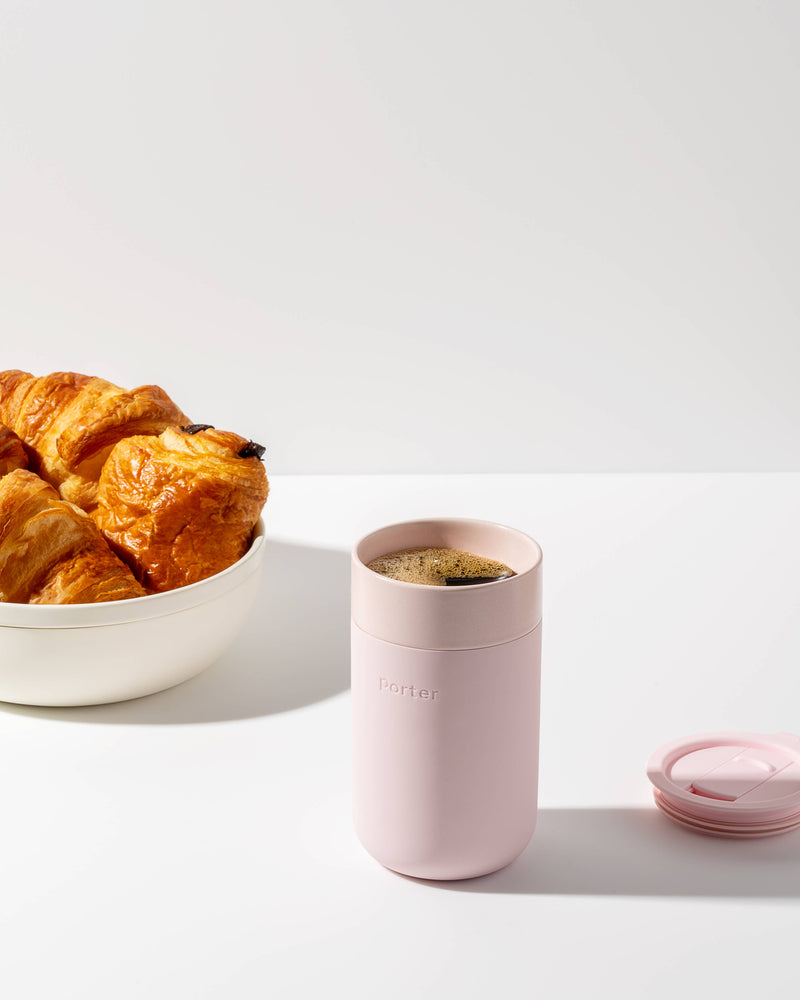 W&P - Ceramic Reusable Coffee Mug 16oz: Charcoal next to a bowl of croissants, showcasing its stylish, eco-friendly design with a silicone sleeve.
