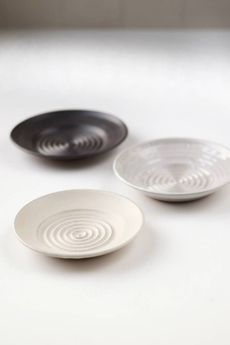 Gravesco Pottery - Garlic Grater Plate in Black, featuring concentric rings for easy garlic preparation and serving, displayed with two other handcrafted ceramic plates.
