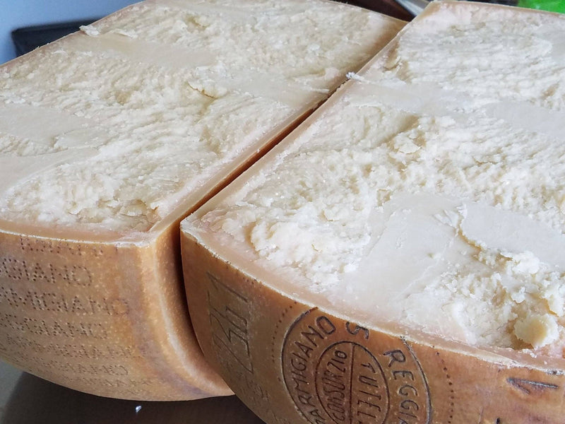 Nicola's Marketplace - Parmigiano Reggiano DOP Mitica® 36 months: 7 Ounces, showing two halved wheels with crumbly interiors, highlighting its certified artisan quality.