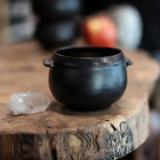 Gravesco Pottery - Black Cauldron Bowl on rustic wood, accompanied by clear-quartz crystal. Perfect for soups and brews, embodying artisanal craftsmanship and Halloween charm.