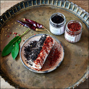 Villa Jerada - Aleppo - 60g jar on a brass tray with goat cheese rolled in Urfa and Aleppo peppers, surrounded by dried chilies and bay leaves.