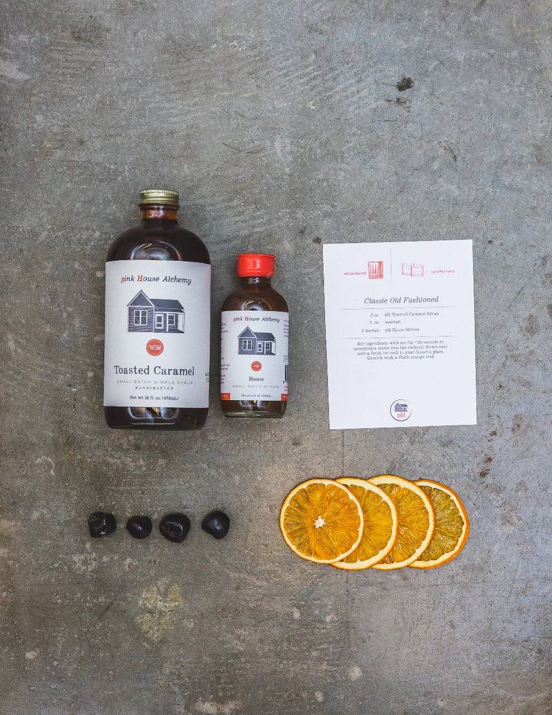 Pink House Alchemy - Toasted Caramel Syrup and cocktail ingredients for a Classic Old Fashioned, featuring syrup, recipe card, cherries, and dehydrated orange wheels.