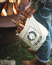 Person holding Farmhouse Pottery - Fatwood - 5lb. Bag filled with kindling sticks, preparing a fire in a firepit outdoors, wearing jeans and sturdy boots.