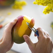 Hands peeling a mango with an Opinel | Essential Small Kitchen Knife Set peeler, showcasing its precision and quality craftsmanship from the Primo set at Athens Cooks.