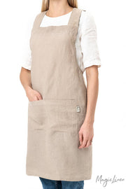 Woman wearing MagicLinen's Pinafore cross-back linen apron with twin-sectioned front pocket, ideal for cooking or gardening, showcasing its functional design and unisex fit.