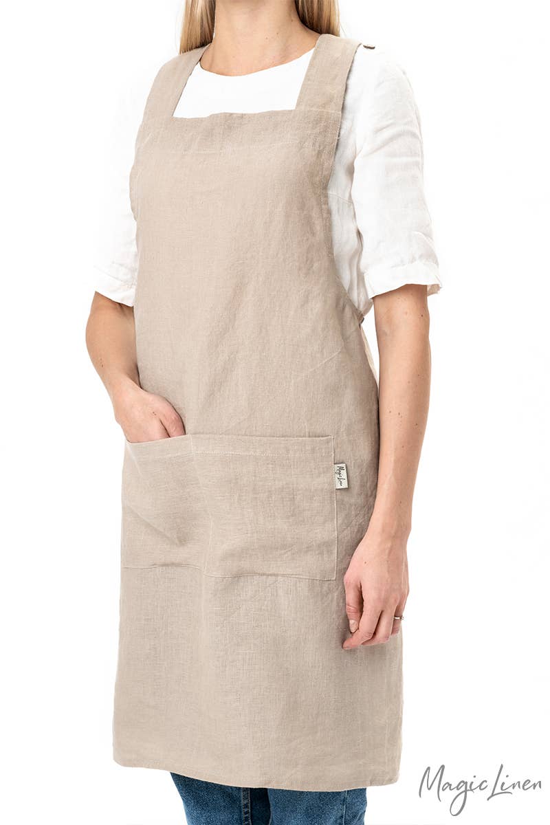 Woman wearing MagicLinen's Pinafore cross-back linen apron with twin-sectioned front pocket, ideal for cooking or gardening, showcasing its functional design and unisex fit.