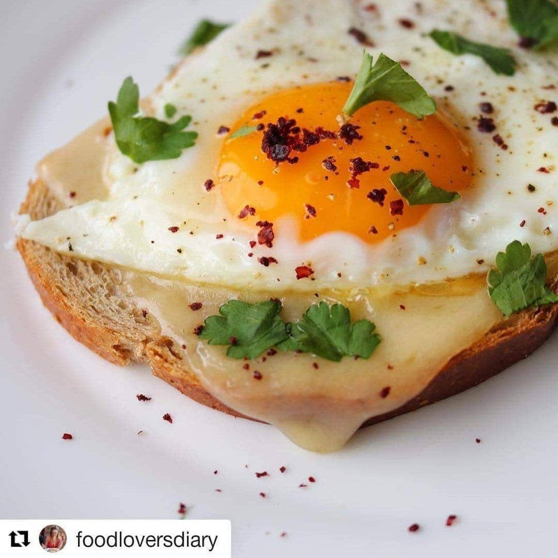 Burlap & Barrel's Cured Sumac seasoning is showcased on a toast with melted cheese, sunny-side-up egg, herbs, and red pepper flakes, highlighting its culinary versatility.