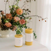 Mo&Co Home - 100% Beeswax Pillar Candles in warm honey-yellow, featuring minimalist labels, set in a clean, airy arrangement with autumnal flowers and greenery.