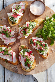 Overhead view of crostini with cheese and radishes, featuring Wholesome Good - Maldon Sea Salt 8.5oz / 12: Single, alongside a bowl of flaky sea salt.