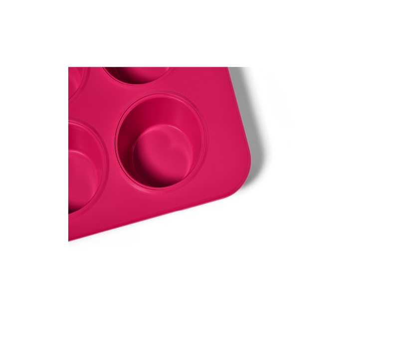 Great Jones | Stud Muffin - Blueberry: Close-up of a pink, nonstick pan designed for baking 12 muffins, featuring even heat distribution and easy cleanup.