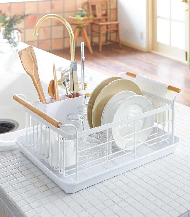 Yamazaki Home | Steel + Wood Dish Rack with Drainer Spout beside sink, holding plates, mugs, glasses, and utensils; wooden handles and towel rail on a drip tray.