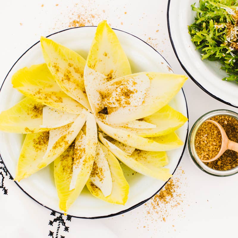 Villa Jerada - Dukkah - 50g seasoning sprinkled over Belgian endive with cheese slices, accompanied by a bowl of salad greens and a jar of Dukkah.