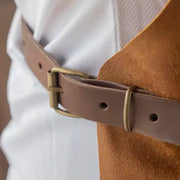 Messermeister - Vintage Leather Apron - Amber, featuring a medium-brown leather belt with brass buckle, styled over a white shirt and camel suede layer.