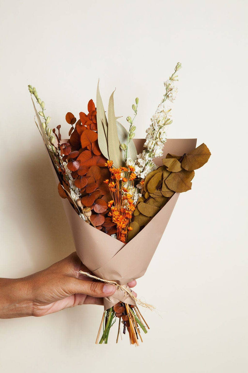 Idlewild Floral Co. - Harvest Dried Flower Mini Bouquet held in hand, featuring preserved eucalyptus, orange blossoms, and seed pods, wrapped in tan paper with twine.