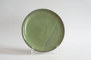 RachaelPots - Dinner Plate: Nude/White displayed on a stand. A simple, round ceramic plate with a muted green glaze, slightly upturned edge, hand-thrown in Brooklyn.